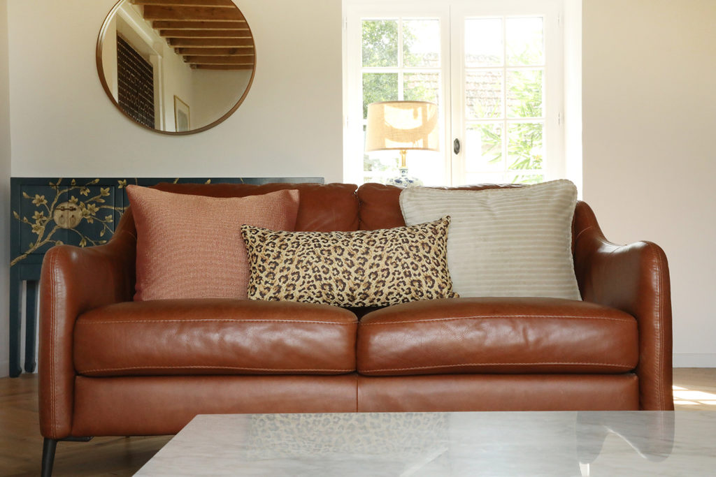Coussins en velours côtelé crème et imprimé léopard sur canapé en cuir marron – Maison du Coussin.