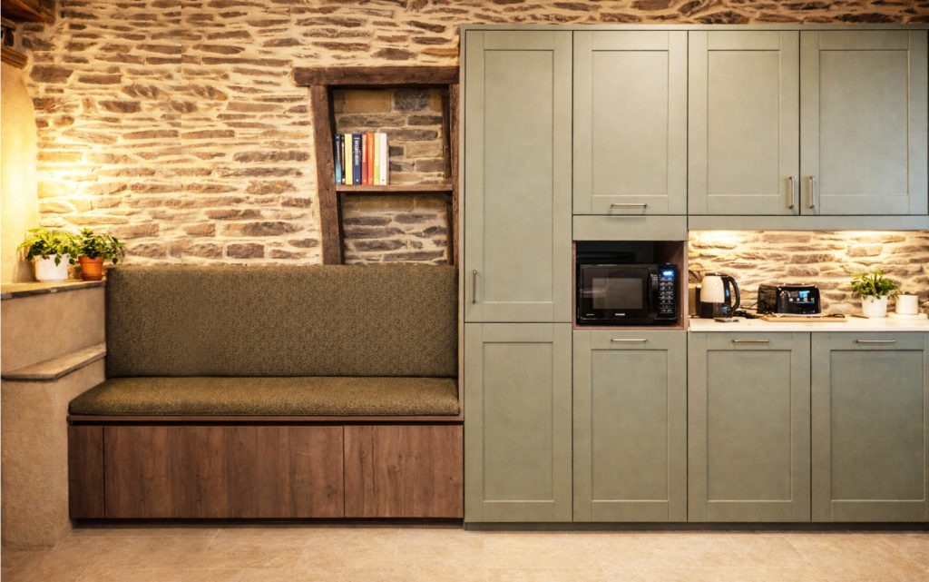 Coussin d’assise et dossier vert kaki en bouclette traitée anti-taches, réalisés sur mesure pour une banquette de cuisine contre un mur en pierre irrégulier dans une maison ancienne à la campagne.