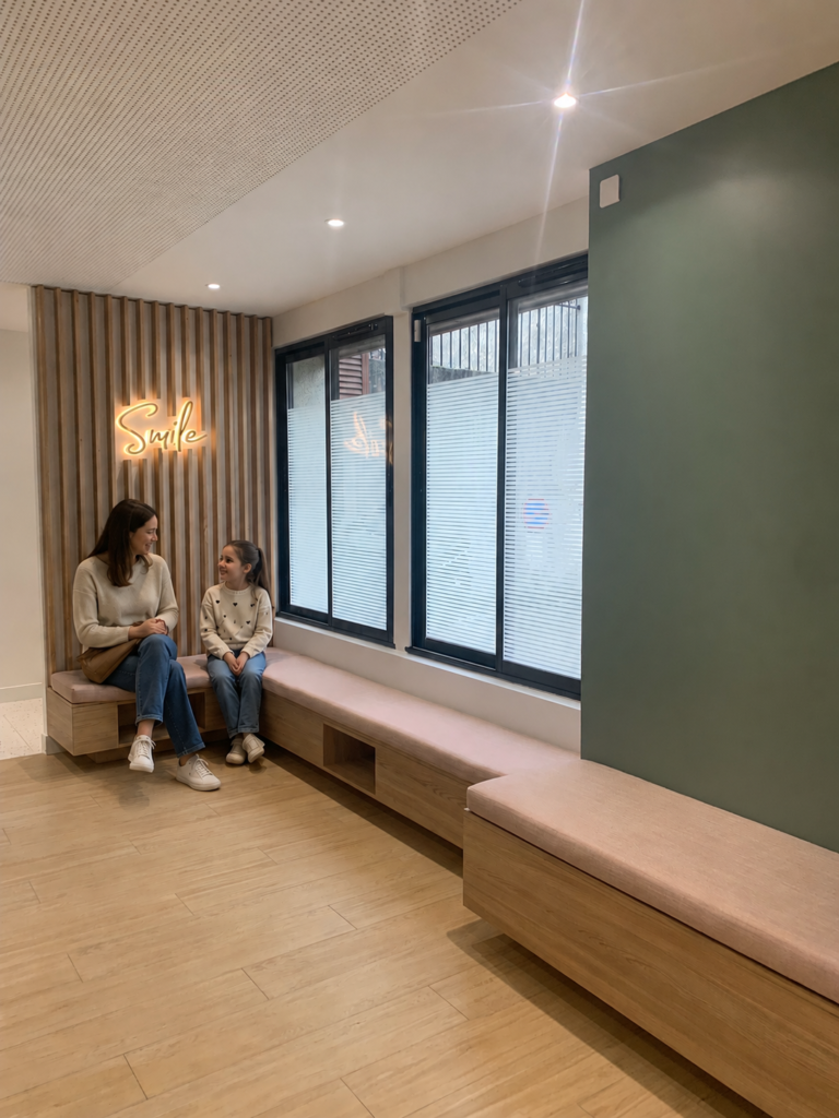 Banquette sur mesure rose poudré dans une salle d’attente chaleureuse de cabinet dentaire, avec touches de bois clair et ambiance apaisante pour les patients.